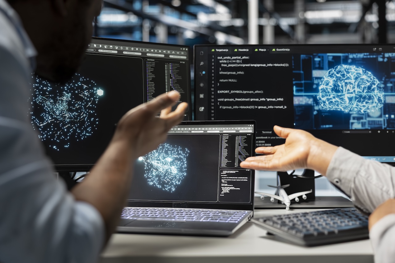 Team tecnico davanti a schermi con interfacce AI, codice e modelli digitali
